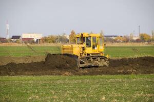 The yellow tractor with attached grederom makes ground leveling. photo