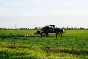 tractor with the help of a sprayer sprays liquid fertilizers on young wheat in the field. photo