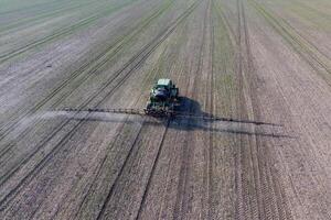 Tractor with hinged system of spraying pesticides. Fertilizing with a tractor, in the form of an aerosol, on the field of winter wheat. photo