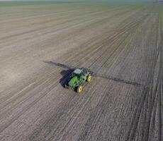 Tractor with hinged system of spraying pesticides. Fertilizing with a tractor, in the form of an aerosol, on the field of winter wheat. photo