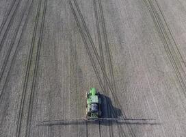 Tractor with hinged system of spraying pesticides. Fertilizing with a tractor, in the form of an aerosol, on the field of winter wheat. photo