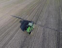 Tractor with hinged system of spraying pesticides. Fertilizing with a tractor, in the form of an aerosol, on the field of winter wheat. photo