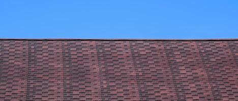 Roof from multi-colored bituminous shingles. Patterned bitumen shingles. Bituminous burgundy roof. photo
