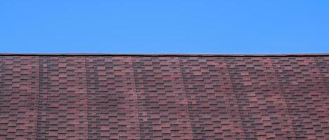 Roof from multi-colored bituminous shingles. Patterned bitumen shingles. Bituminous burgundy roof. photo