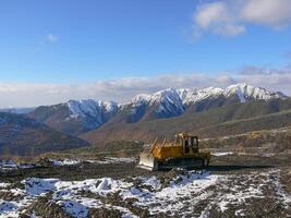 Crawler tractor with grederom against the backdrop of snow-capped mountains photo