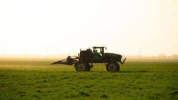 tractor en el puesta de sol antecedentes. tractor con alto ruedas es haciendo fertilizante en joven trigo. foto