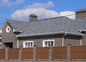 Asphalt shingle. Decorative bitumen shingles on the roof of a brick house. Fence made of corrugated metal. photo