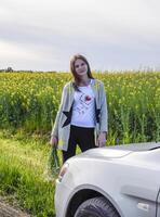 un hermosa joven mujer con un ramo de flores de margaritas soportes cerca un plata coche foto