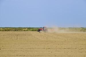 Tractor with a grader aligns the soil on the field. The tractor raised dust. photo