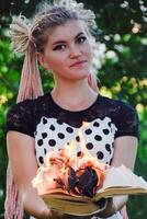 girl holds a burning book in her hands. A young woman in a forest burns a book. photo