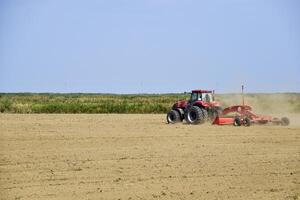 Tractor with a grader aligns the soil on the field. The tractor raised dust. photo