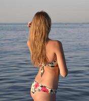 rubio niña en un bikini en pie en el mar agua. hermosa joven mujer en un vistoso bikini en mar antecedentes foto