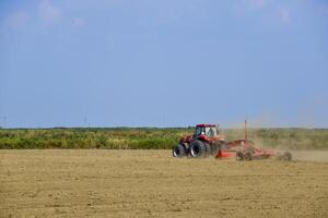 Tractor with a grader aligns the soil on the field. The tractor raised dust. photo