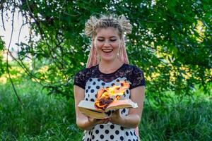 girl holds a burning book in her hands. A young woman in a forest burns a book. photo