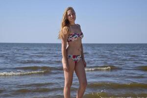 Blond girl in a bikini on the beach. Beautiful young woman in a colorful bikini on sea background photo