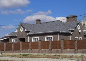 Asphalt shingle. Decorative bitumen shingles on the roof of a brick house. Fence made of corrugated metal. photo