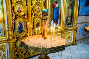 Orthodox church from the inside. Burning wax candles in front of icons and frescoes. Christian religion. photo