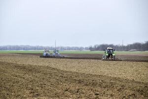 lozano y aflojar el suelo en el campo antes de siembra. el tractor arados un campo con un arado foto