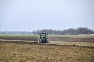 lozano y aflojar el suelo en el campo antes de siembra. el tractor arados un campo con un arado foto