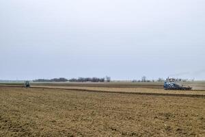 Lush and loosen the soil on the field before sowing. The tractor plows a field with a plow photo