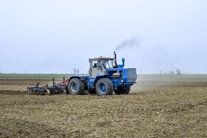 lozano y aflojar el suelo en el campo antes de siembra. el tractor arados un campo con un arado foto