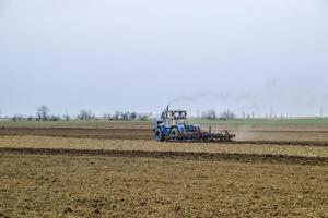 lozano y aflojar el suelo en el campo antes de siembra. el tractor arados un campo con un arado foto