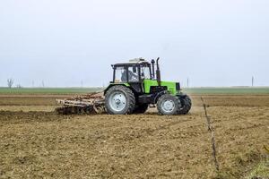 lozano y aflojar el suelo en el campo antes de siembra. el tractor arados un campo con un arado foto