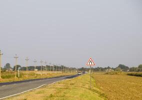 interurbano camino. firmar de estrechamiento el la carretera. el asfalto la carretera y el herboso lado de el la carretera. foto