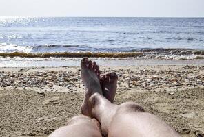 el piernas de un hombre en un playa antecedentes. un hombre mentiras en un amatraza en el playa y es descansando piernas en el marco. foto