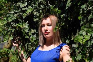 Portrait of a girl in a blue dress on background of green arbor of ivy. photo