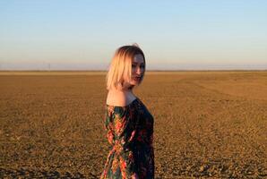 Woman in a plowed field in a red-black dress on a sunset background. photo