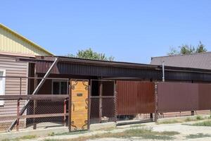 Brick house with a fence and gates. View of a new built-up fence and a house made of bricks and corrugated metal. photo