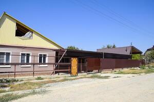 Brick house with a fence and gates. View of a new built-up fence and a house made of bricks and corrugated metal. photo