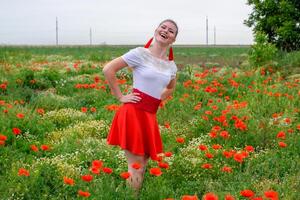 Blonde young woman in red skirt and white shirt, red earrings is in the middle of a poppy field. photo