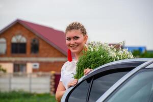 Girl with a bouquet of daisies sits in car. photo