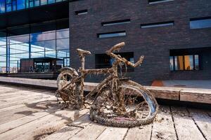 oxidado bicicleta descansa en paseo marítimo frente a un moderno urbano edificio fachada foto