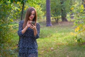 Pretty woman writes a message, looks at the phone, trees in a forest park photo