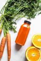 Freshly squeezed carrot juice in a bottle and fresh carrots on a white marble background photo