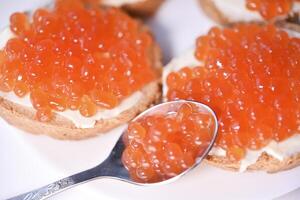 rojo salmón caviar en un pan y manteca. un cuchara con rojo caviar. foto