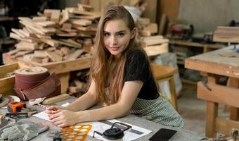 un joven mujer es formación a ser un carpintero en el taller. ella trabajos con un ordenador portátil computadora en un madera taller. hembra carpintero contacto clientes por teléfono inteligente SME pedidos, puesta en marcha y pequeño foto