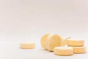 Tablets with a yellow tint with small inclusions of visible raw materials on a white creamy pastel background. Close-up. Selective focus. Theme is treatment of diseases, medicine and pharmaceuticals. photo