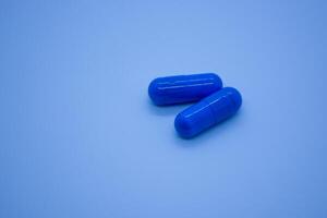 Two blue pills on blue background. Focus on foreground, shallow DOF. Close-up. Theme is treatment of diseases, medicine and pharmaceuticals. photo