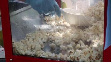 Classic popcorn machine with an unknown hand scooping fresh popcorn. Popcorn is poured into a bag for guests to enjoy. Manufacturer of popcorn and scoop. video