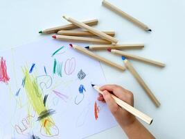 pequeño niño sorteos con de colores lapices en papel en blanco mesa. foto