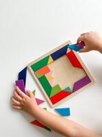 childs hand collects multicolored wooden mosaic on white background. photo