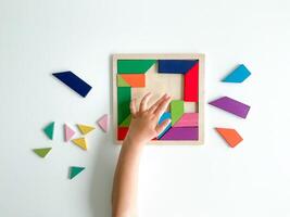 niños mano recoge multicolor de madera mosaico en blanco antecedentes. niño resuelve vistoso tangram foto