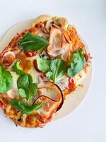 Pizza with ham, mozzarella, tomatoes and leaves on a white background. View from above photo