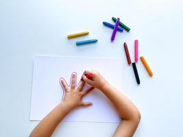 para niños manos dibujar su mano con cera lápices de color en blanco papel, parte superior vista. foto