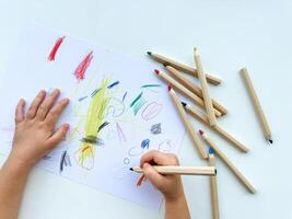 pequeño niño sorteos con de colores lapices en papel en blanco mesa. foto