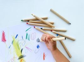small child draws with colored pencils on paper on white table. photo